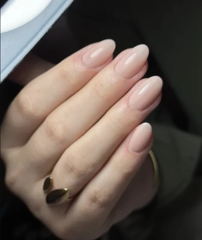 Ongles nude en forme d'amande, portés avec une bague dorée