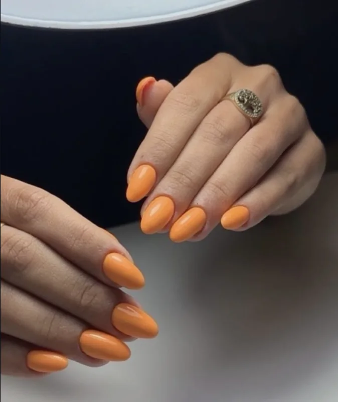 Pose permanente orange sur ongles en amande, avec une bague ancienne