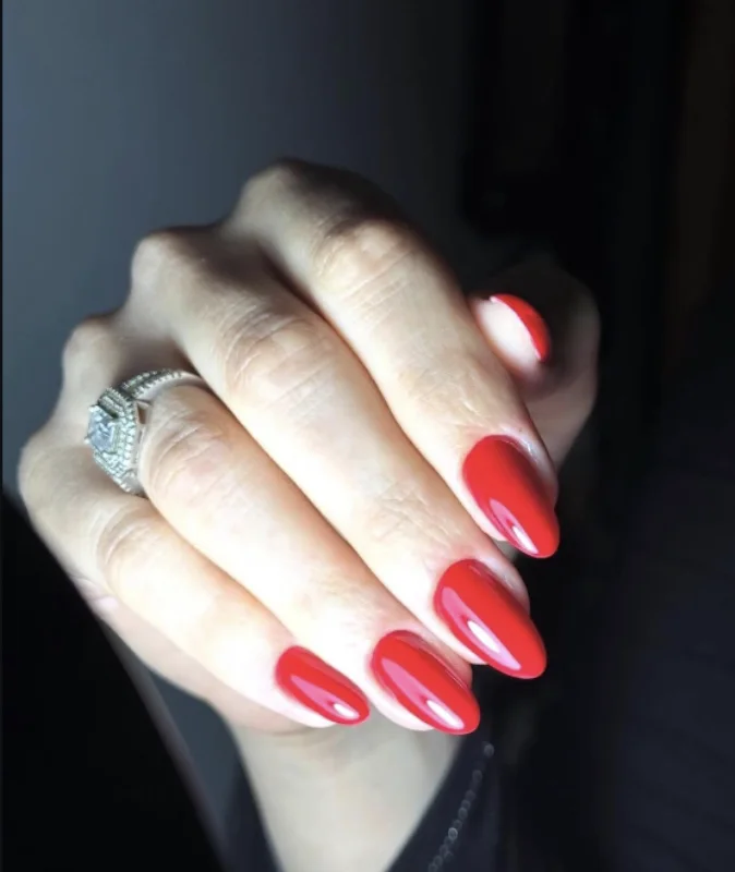 Pose permanente rouge vif sur ongles en amande, avec des bagues