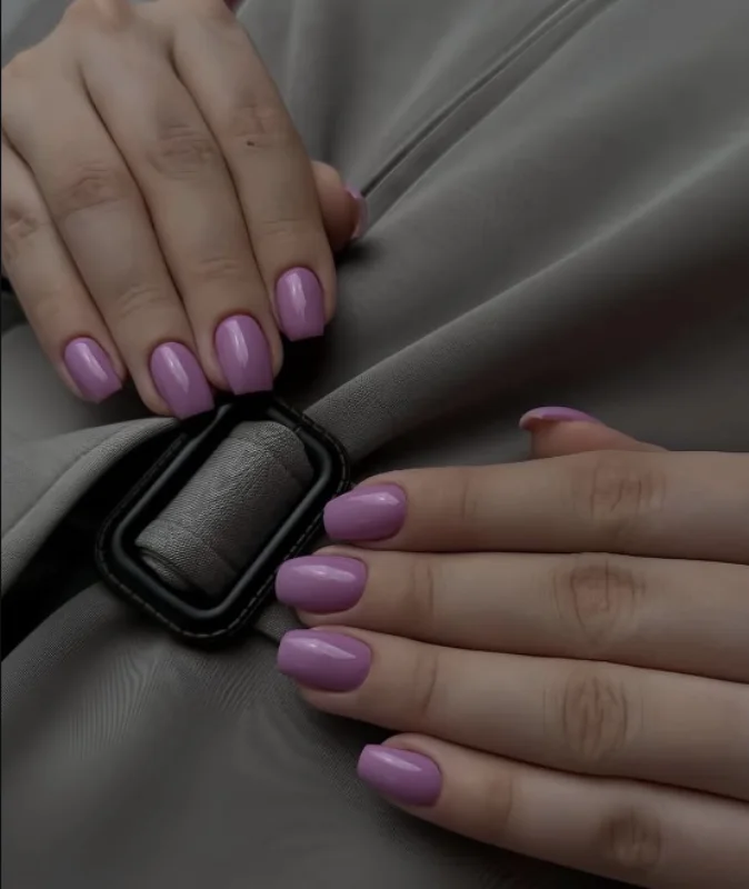 Pose permanente mauve sur ongles courts, mains posées sur un sac