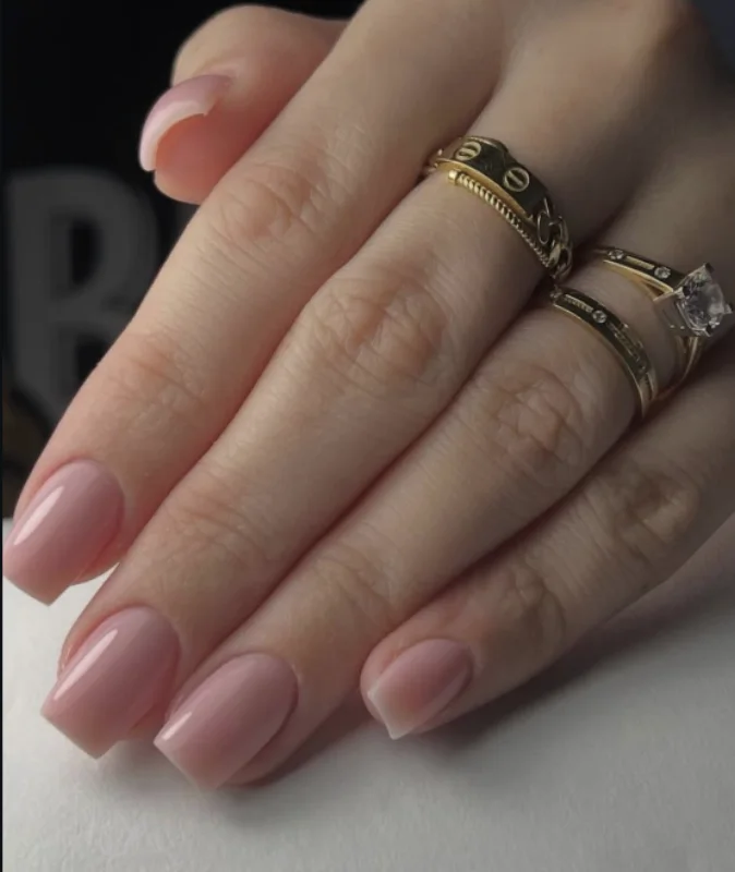 Pose nude rosée sur ongles carrés, portée avec plusieurs bagues dorées