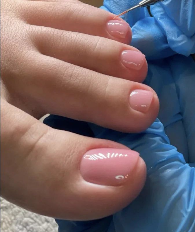 Pose en cours sur les ongles des pieds, la prothésiste porte des gants