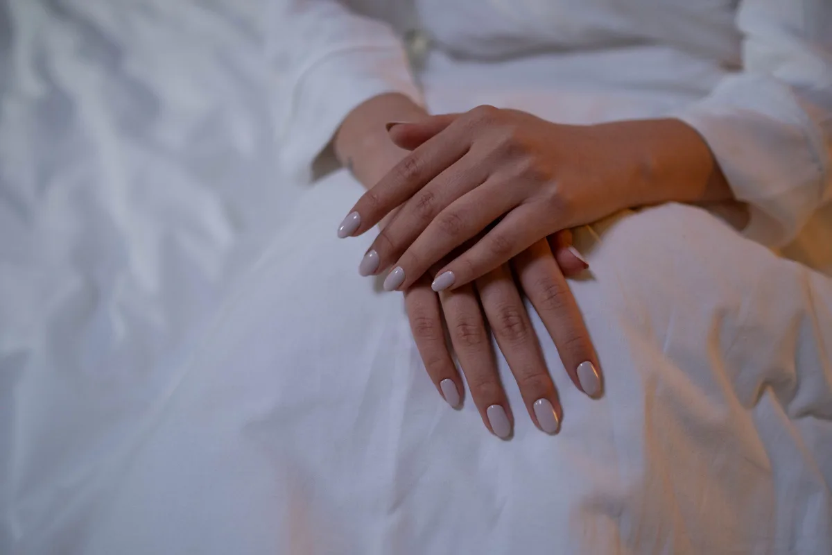 Mains posées sur un tissu clair, ongles nude parfaitement limés