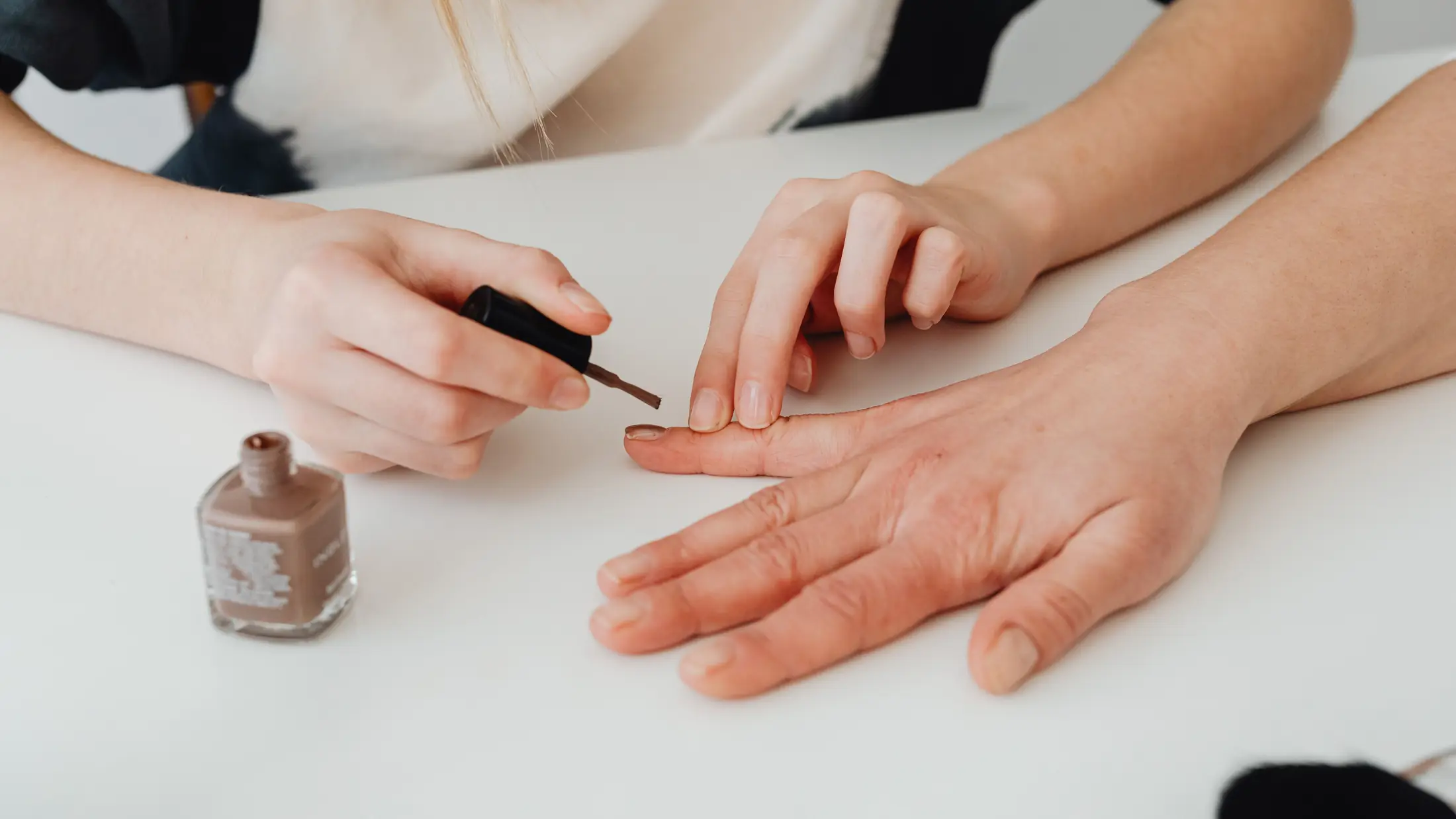 Pose de vernis en cours, mains posées sur une table claire